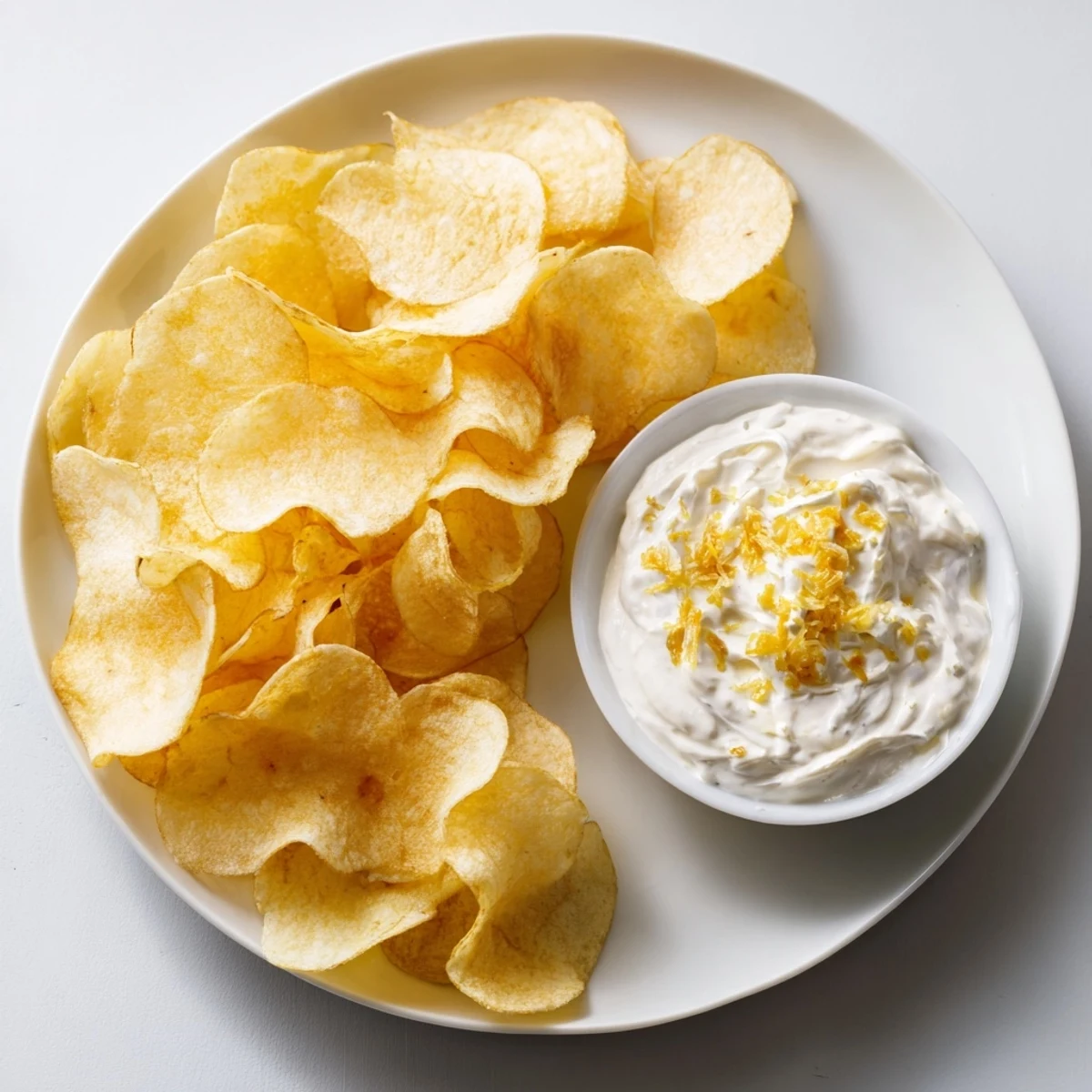 Golden-brown potato chips surround the creamy onion dip, ideal for an easy snack.