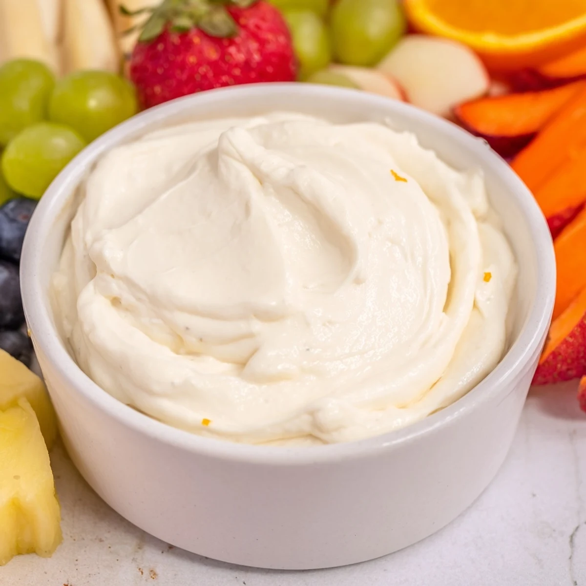 A view of a beautiful bowl of cream cheese fruit dip with fresh, enticing fruit on display.