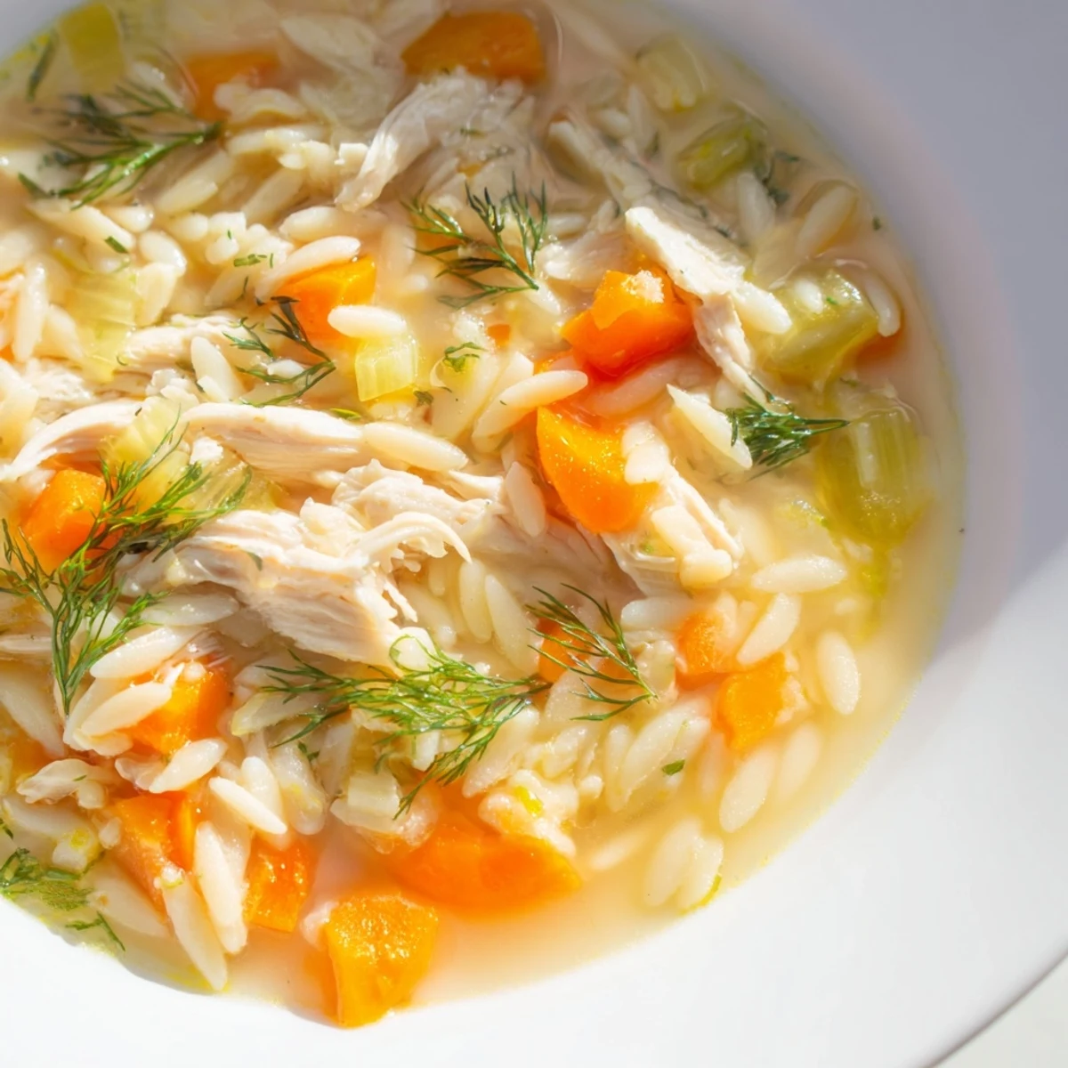 Tender shredded chicken and bright lemon zest float in a steaming bowl of Chicken Lemon Orzo Soup with fresh dill.  