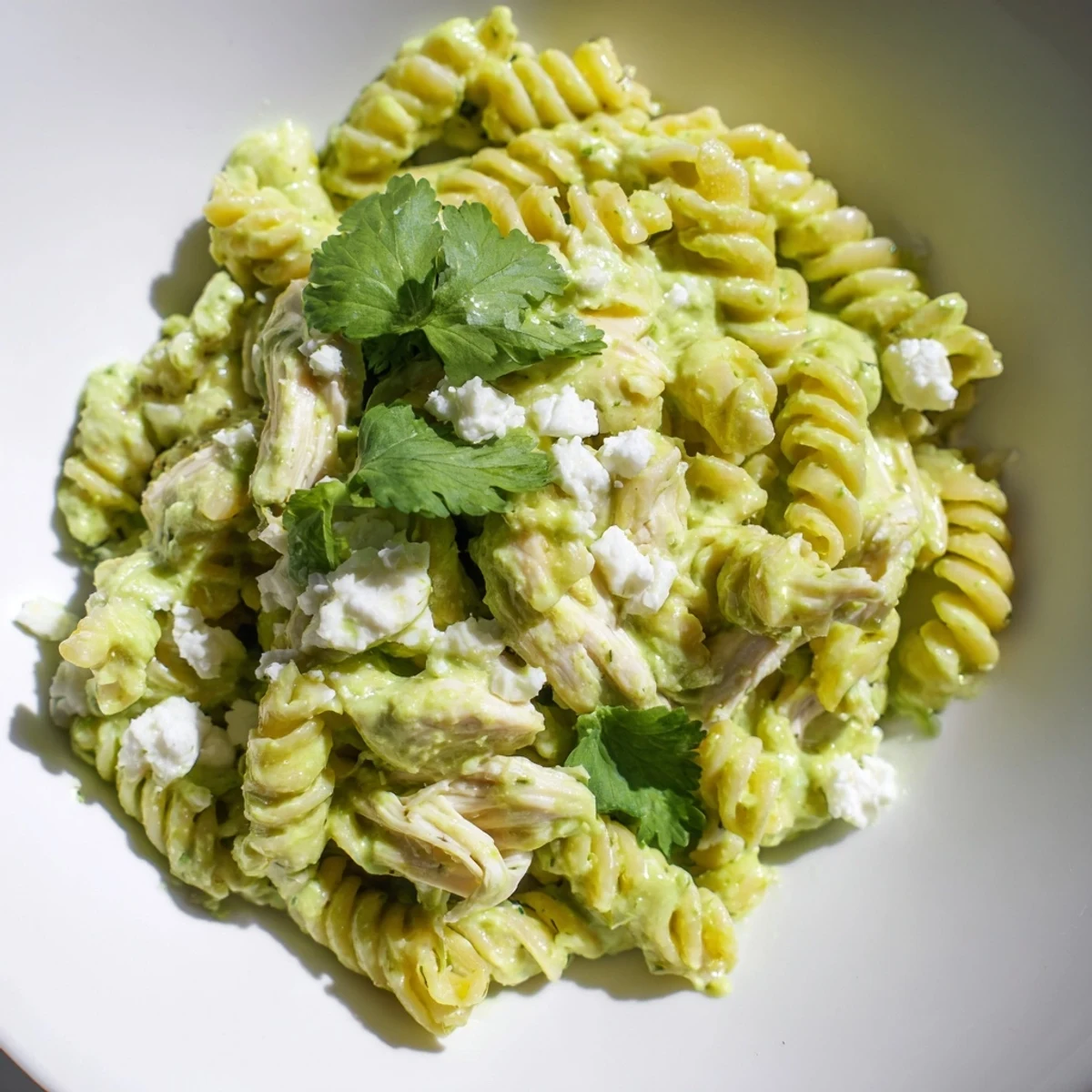 A vibrant bowl of Cilantro Lime Chicken Pasta features rotini and tender shredded chicken coated in a creamy, bright green yogurt sauce.  