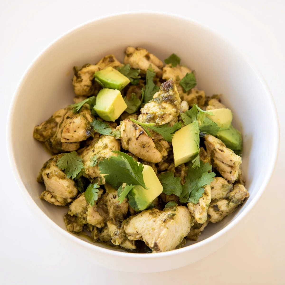 A bowl of homemade Chicken Chili Verde simmered with charred tomatillos and peppers, topped with diced avocado and sliced radishes for crunch.