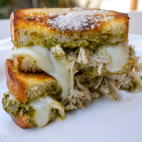 Golden-brown grilled cheese sandwich with shredded chicken, melted mozzarella, and vibrant basil pesto on sourdough.