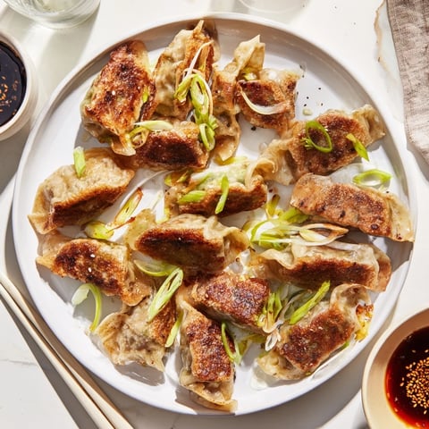 Golden-brown smashed gyozas sizzle in a skillet, showcasing crispy bottoms filled with savory pork and napa cabbage.