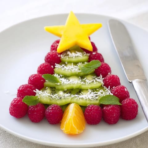 A vibrant Christmas tree fruit plate: ripe kiwi and juicy red raspberries on a platter.