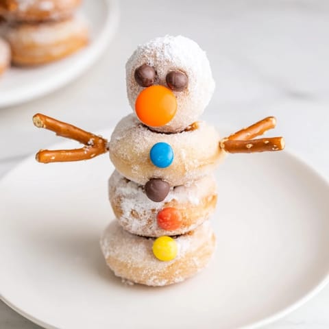 Homemade mini donut snowmen with chocolate chip smiles and pretzel arms, ready to eat.