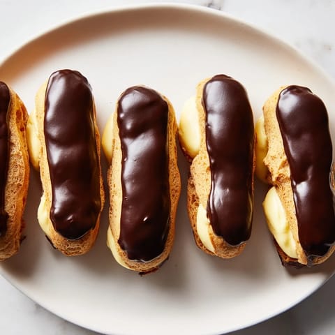 Mini chocolate éclairs in a row: imagine golden pastries filled with creamy vanilla, topped with rich chocolate.
