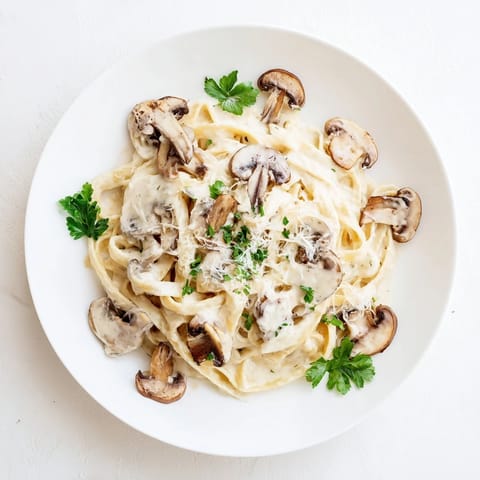 Golden, sautéed cremini mushrooms glisten atop fettuccine coated in a rich, velvety Creamy Mushroom Alfredo sauce garnished with fresh parsley.