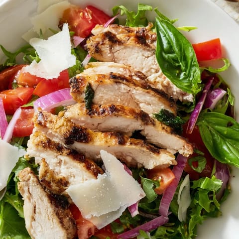 Freshly grilled chicken salad features a colorful bruschetta topping and shaved Parmesan, perfect for a light lunch.  