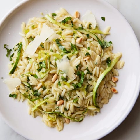 A close-up of the Asparagus Lemon Orzo Salad shows strands of orzo tangled with crisp green ribbons, creamy Parmesan shavings, and a glistening lemon vinaigrette.