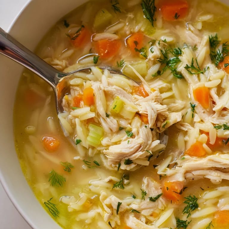 Spoonfuls of orzo pasta and diced carrots swim in a clear, golden broth of Chicken Lemon Orzo Soup.  
