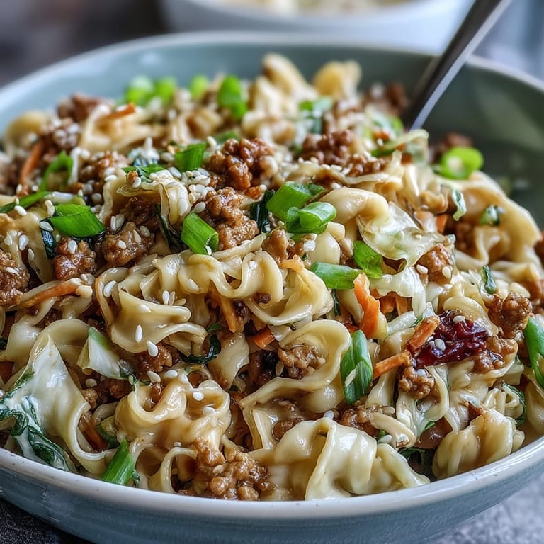 A close-up view of Creamy Potsticker Noodle Stir-Fry served in a bowl, garnished with sesame seeds and fresh green onions.
