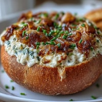 Creamy caramelized onion dip served in a warm sourdough bread bowl, garnished with fresh chives and ready for dipping.  