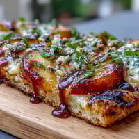Grilled flatbread with BBQ sauce, Brie cheese, and sweet peaches, topped with red onion and fresh basil.